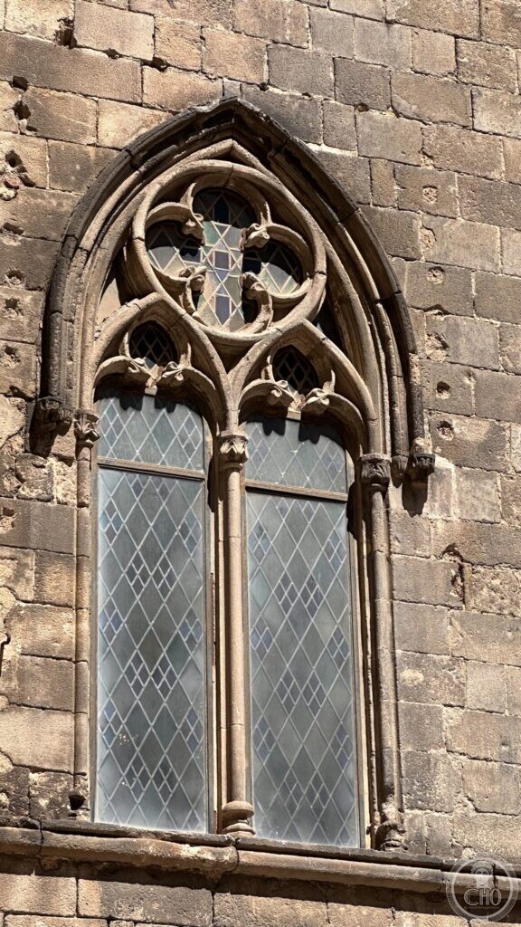A Gothic two-light window with carved tracery set in a rough stone wall