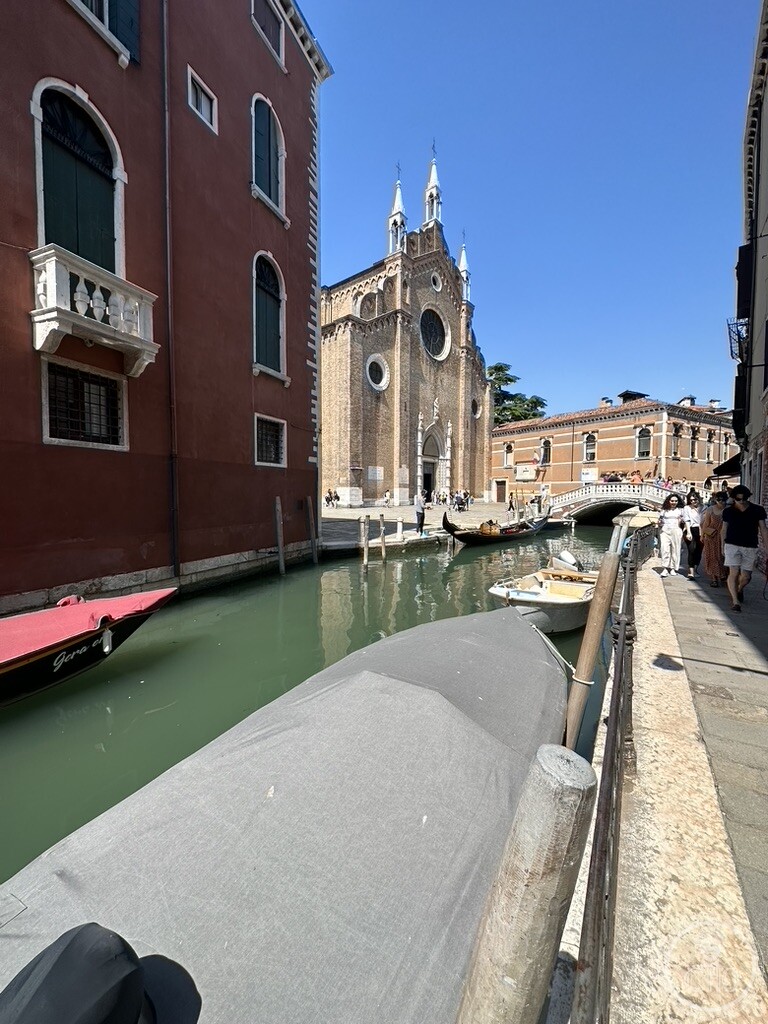 Looking along the Rio dei Frari between house fronts towards the basilica and the bridge, boats moored under covers along the fondamenta