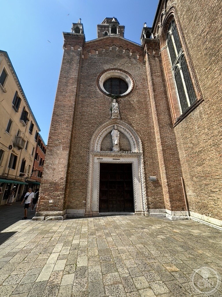 A pointed marble portal on the brick flank of the Frari basilica in Venice, the rose window above it