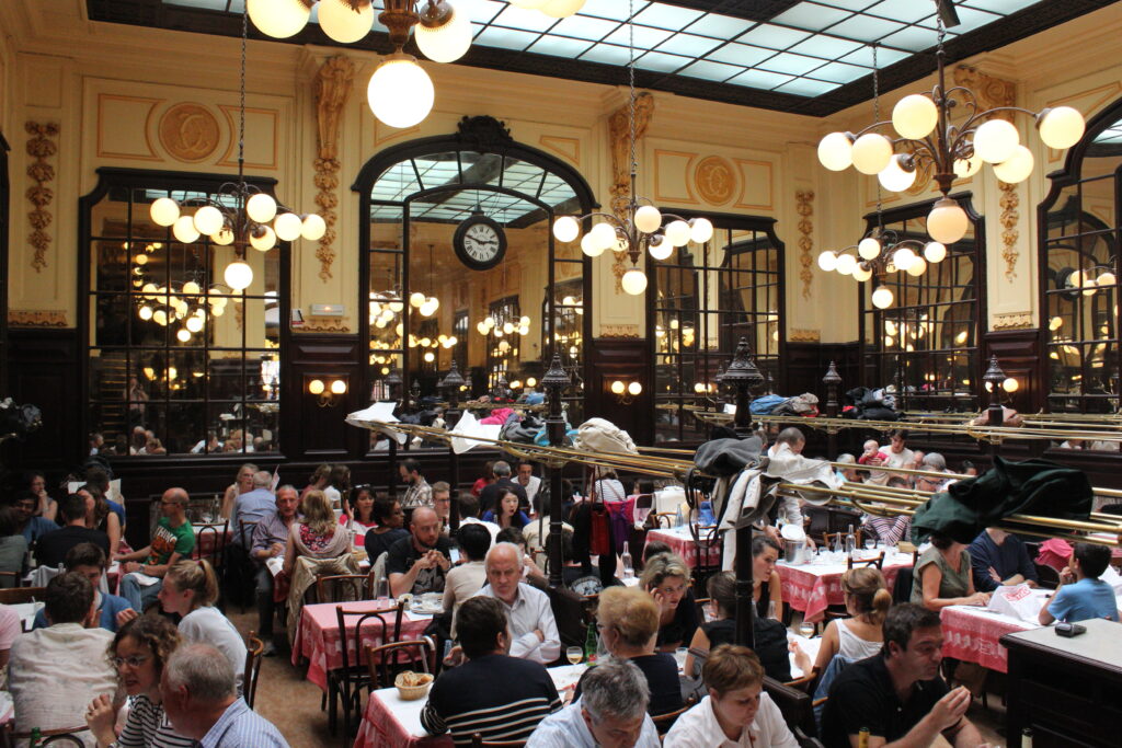 The dining room of Bouillon Chartier in Paris, with carved panelling, brass racks and a glass ceiling