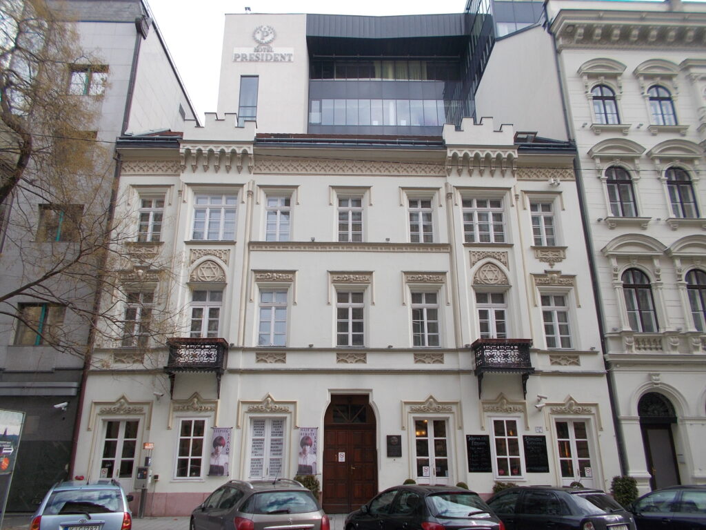 Pale Gothic-Romantic town house with two crenellated gables and Stars of David over the windows, the Hotel President rising behind, Hold utca 5, Budapest
