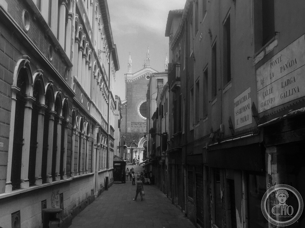 Black and white architectural perspective down Calle Larga Giacinto Gallina framing the Gothic facade of Santi Giovanni e Paolo in Venice