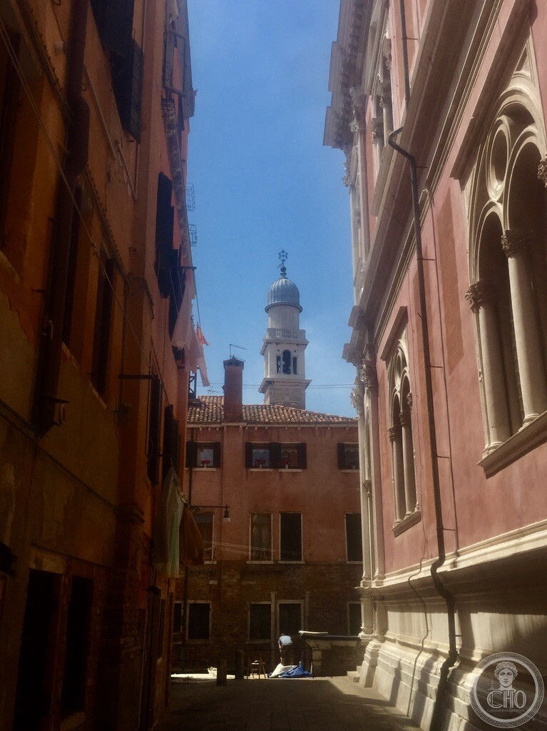 Looking down a sunlit Venetian calle beside a Gothic palazzo towards the distant campanile near Ponte dei Pugni in Venice