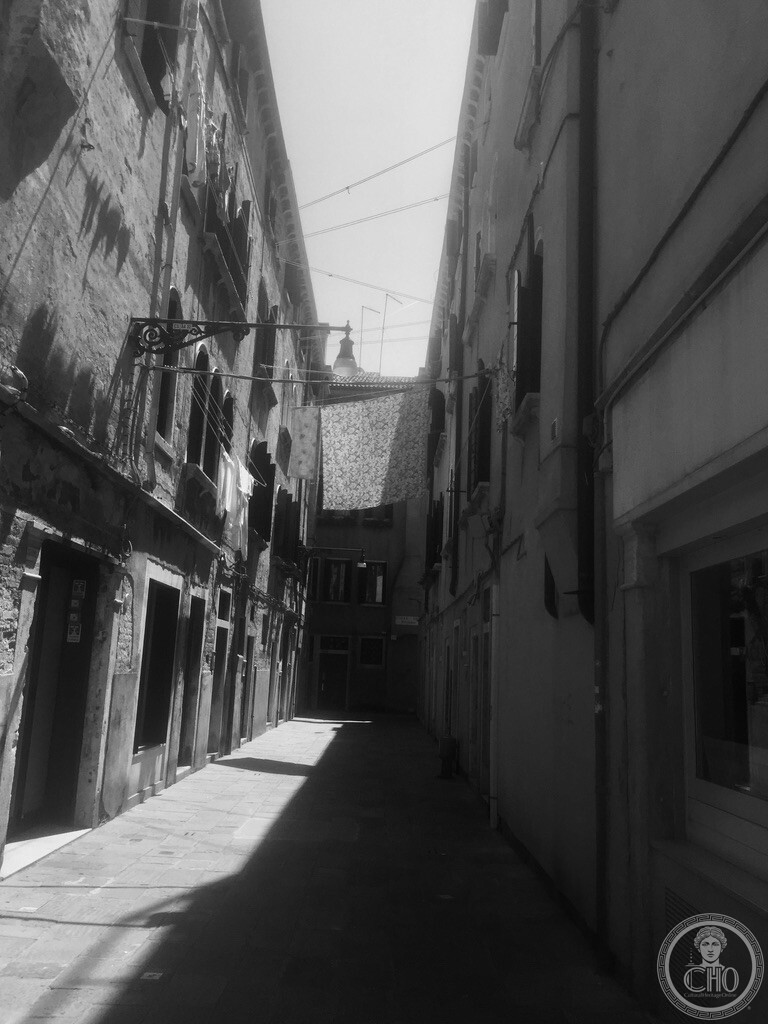 Black and white perspective down the narrow Calle Seconda del Cristo in Castello Venice with laundry hanging overhead between historic buildings