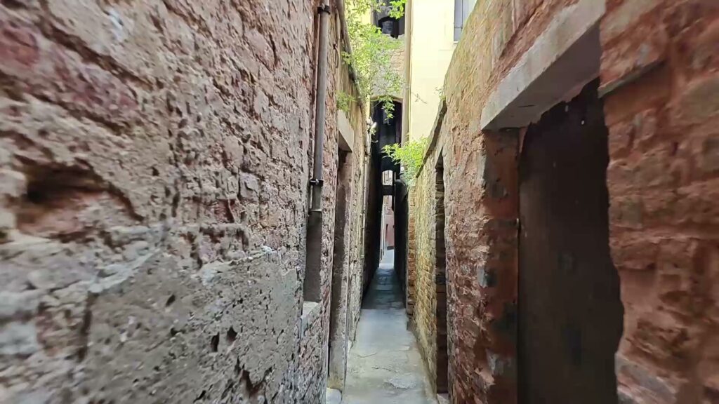 A Venetian alley narrowing between brick walls to a gap barely wider than a shoulder