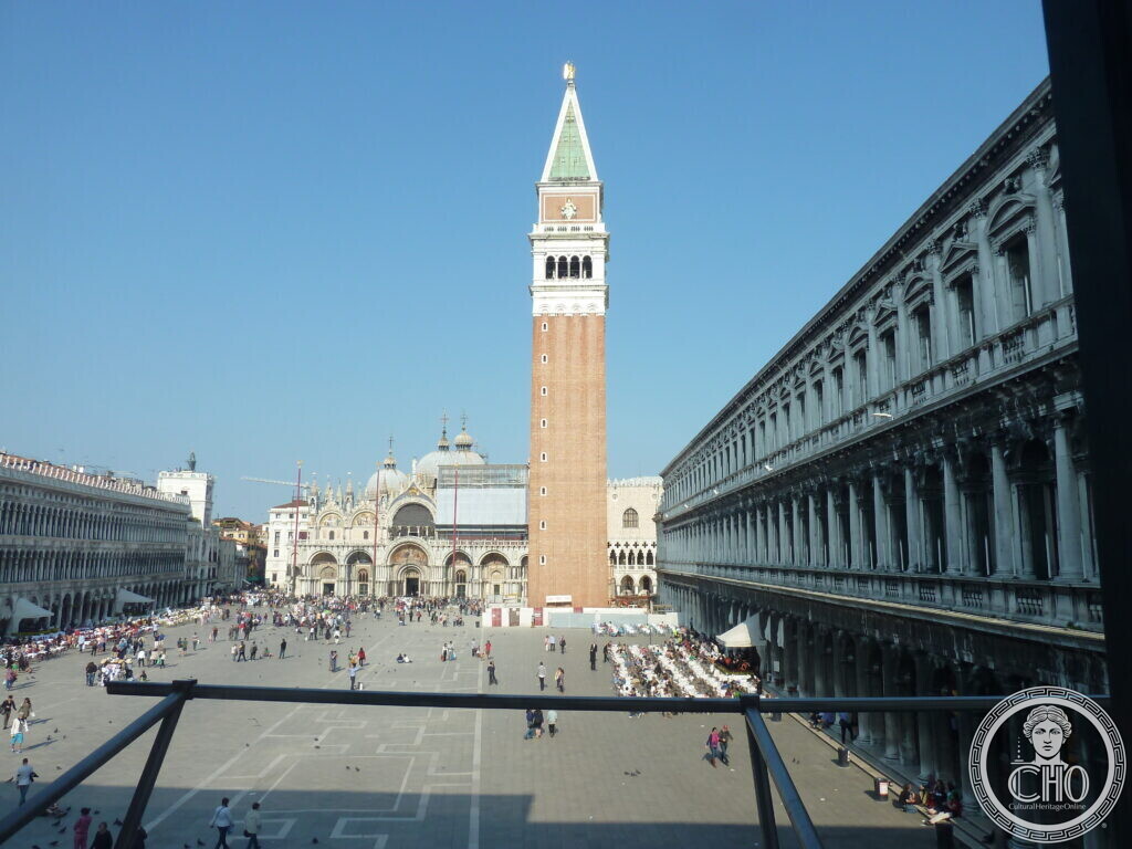 Piazza San Marco seen from a raised window of the Procuratie, the brick shaft of St Mark's Campanile at the centre, the basilica under scaffolding at the far end and the arcades running down both sides