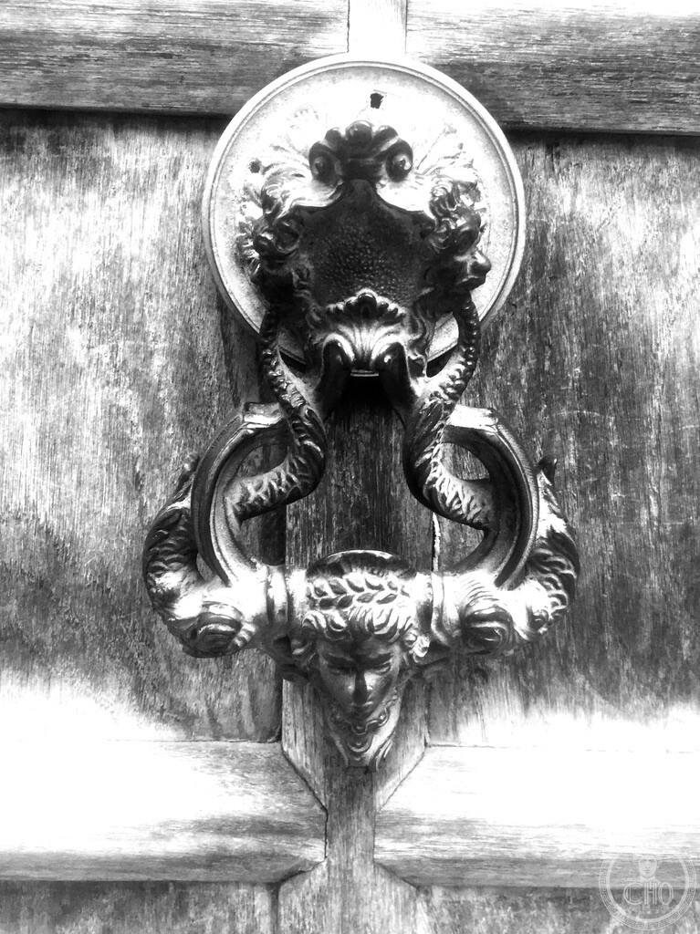 Elaborate antique bronze door knocker on weathered wood depicting twin dolphins and a classical maiden head in Cannaregio