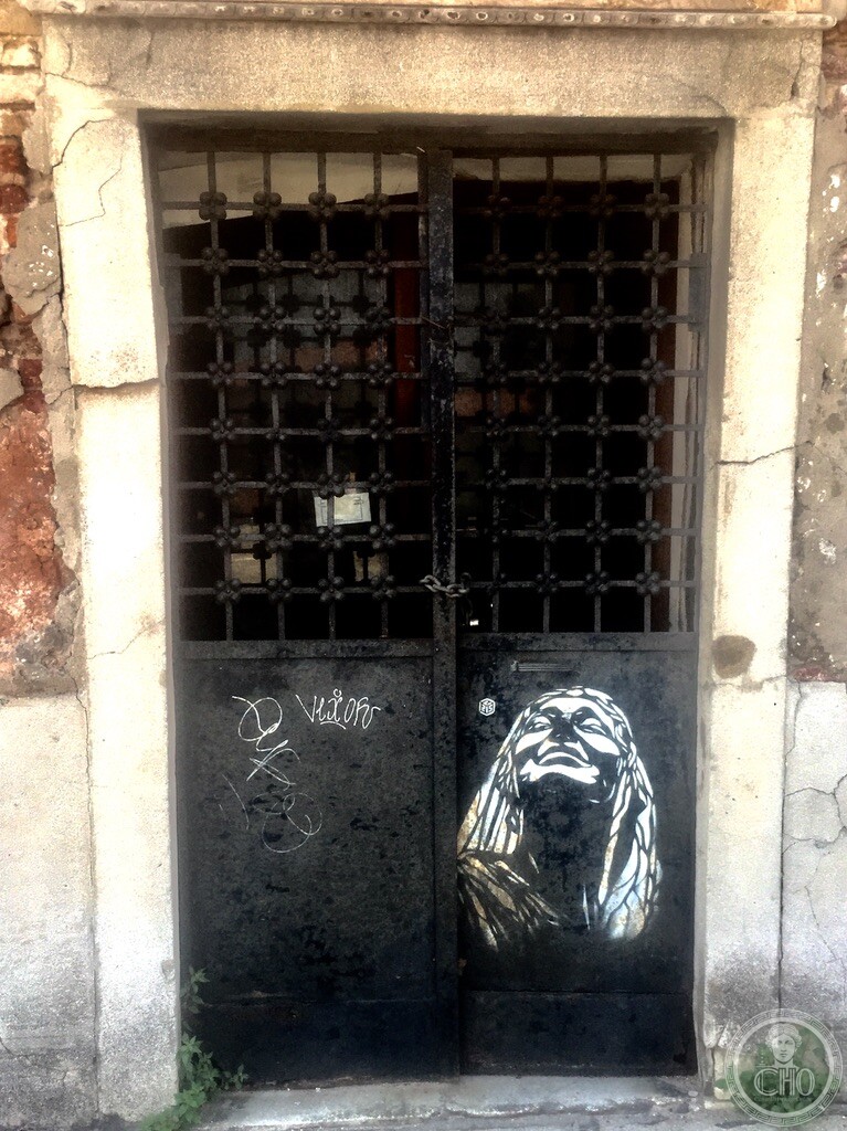 Urban stencil street art of a woman looking upward on an antique wrought-iron gated portal at Campo San Basegio in Dorsoduro Venice