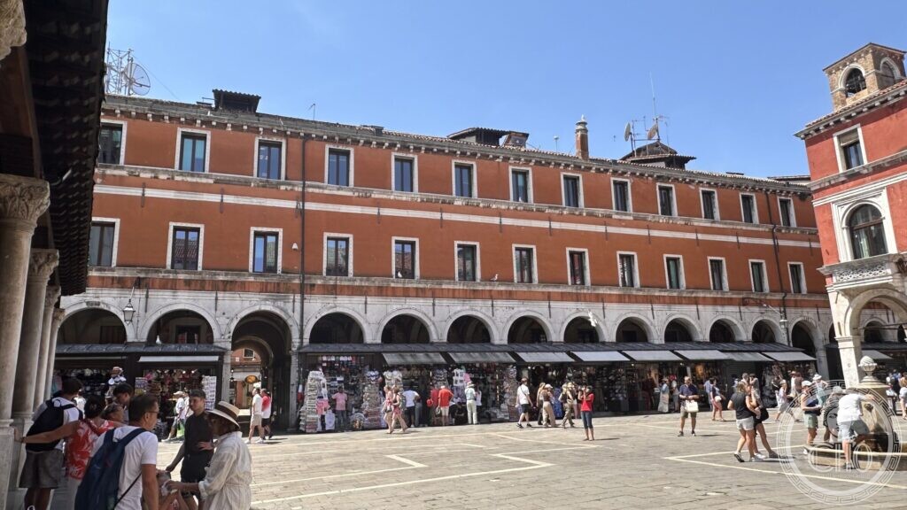 Stalls and shopfronts under the arcades of the campo, with visitors walking past