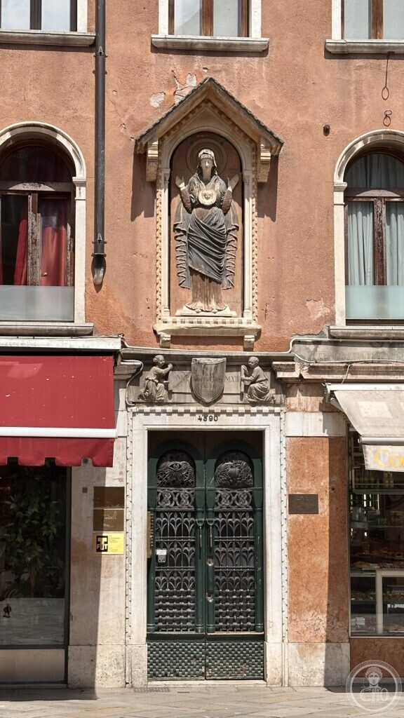 A carved stone relief of a robed figure in a niche above an ornate ironwork door on Campo San Luca