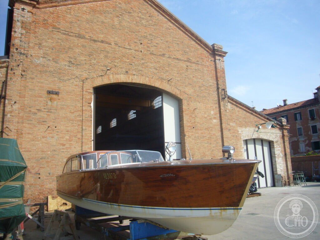 Varnished wooden Venetian motor launch on trestles outside the brick shed of Cantiere Crea