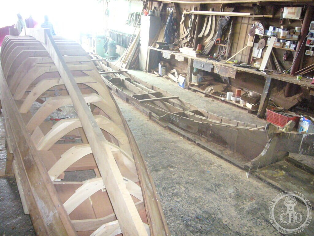 Upturned boat hull showing its timber frames beside the workbenches of Cantiere Crea