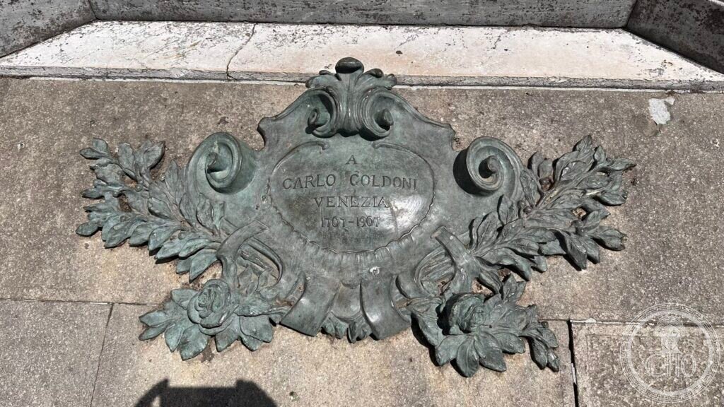 Bronze cartouche with the name of Carlo Goldoni, framed by foliage, set into the stone of the pedestal