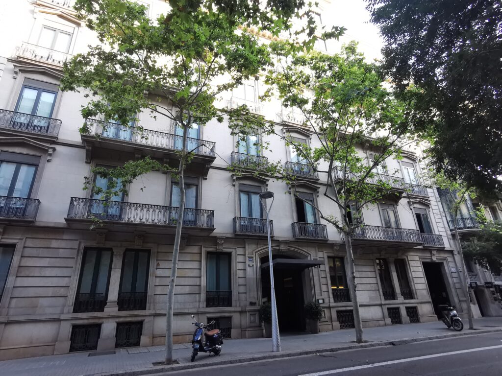Long stone front of Carrer de Mallorca 269 in Barcelona, with a rusticated ground floor, an arched entrance under a black canopy and rows of iron balconies on the upper floors, partly hidden by street trees