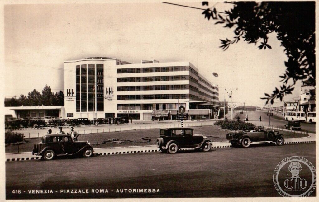 A period postcard of the Autorimessa in Piazzale Roma, Venice, the white garage with its tall glazed stair tower, vintage cars on the square in front