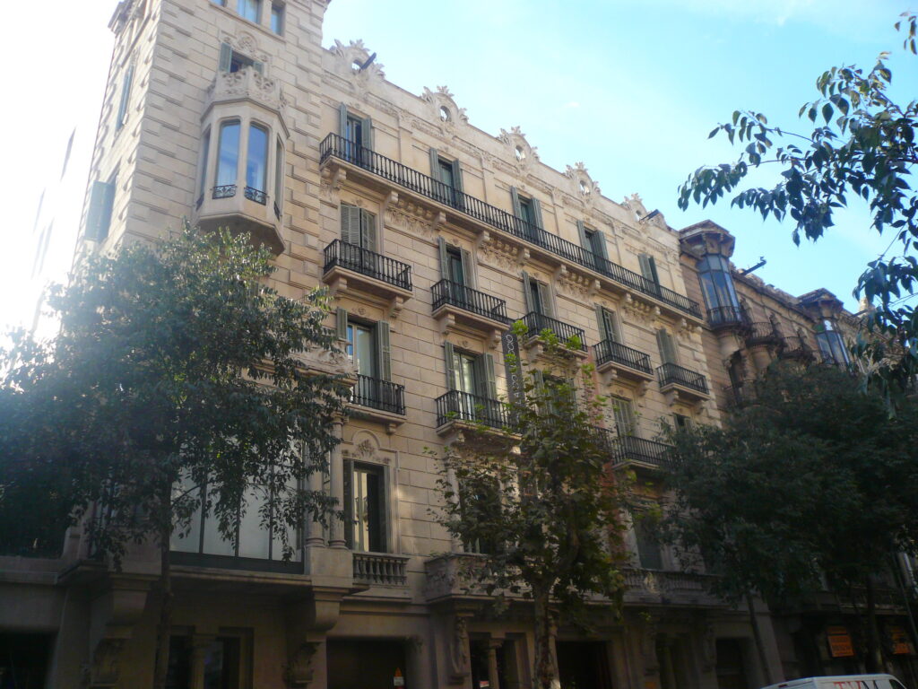 Stone facade with a corner tower and bay window, wrought-iron balconies, green shutters and an ornate crowning, Carrer de la Diputació 250, Barcelona