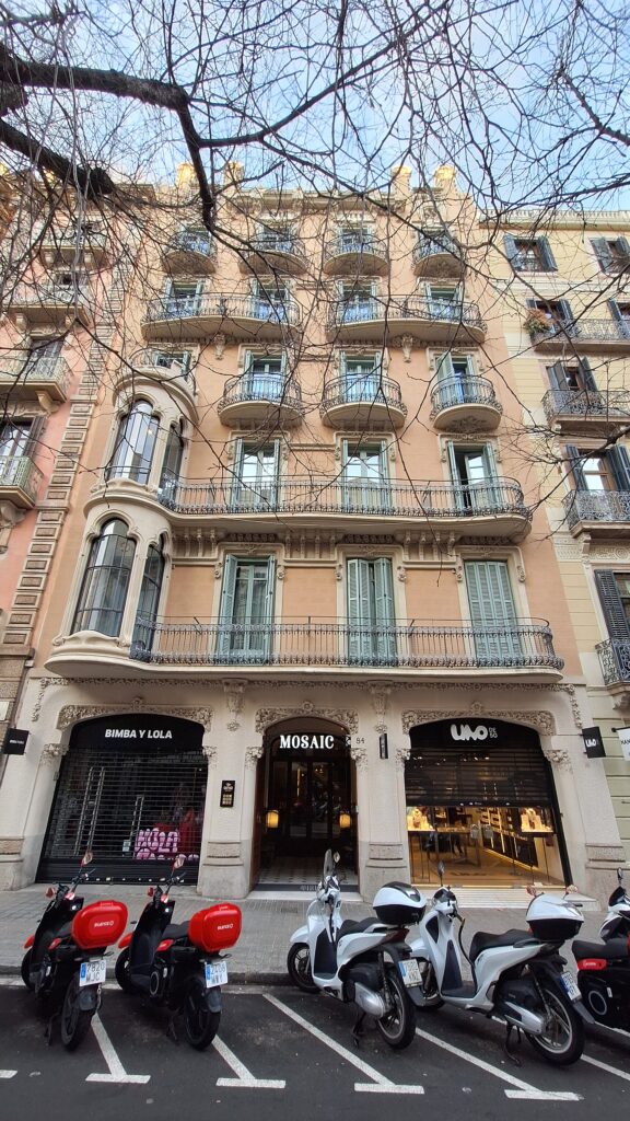 Six-storey modernista front at Rambla de Catalunya 84, Barcelona, with three carved stone arches on the ground floor, the central one lettered Mosaic, a rounded glazed tribune on the left and curved iron balconies on the upper floors