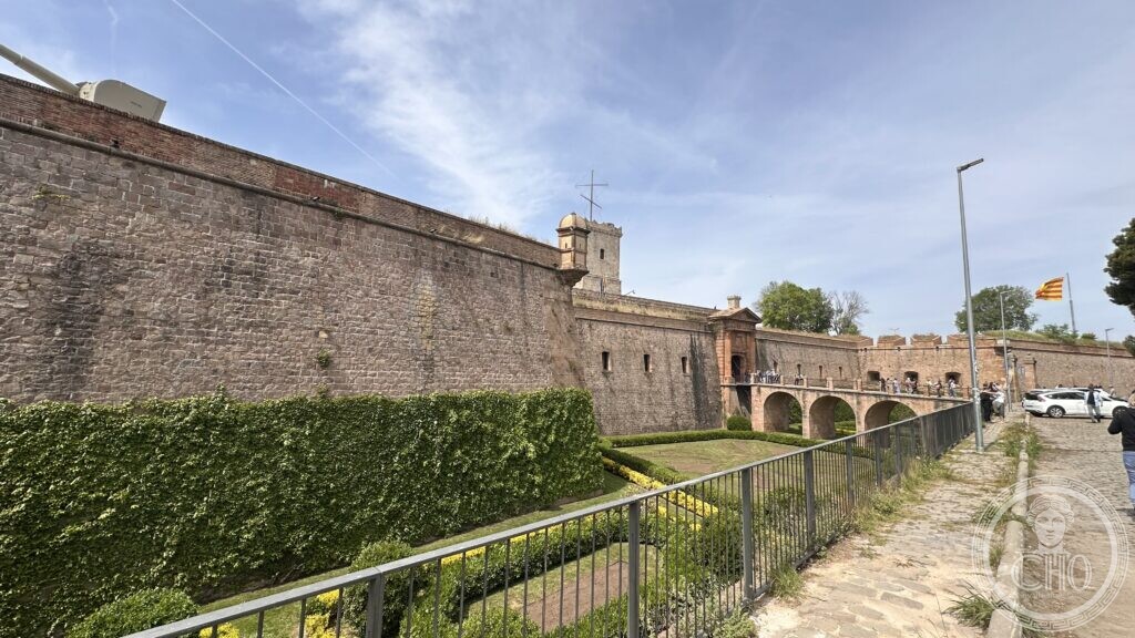 The star-shaped stone bastion walls of Castell de Montjuïc with the dry moat garden below and a Catalan flag flying