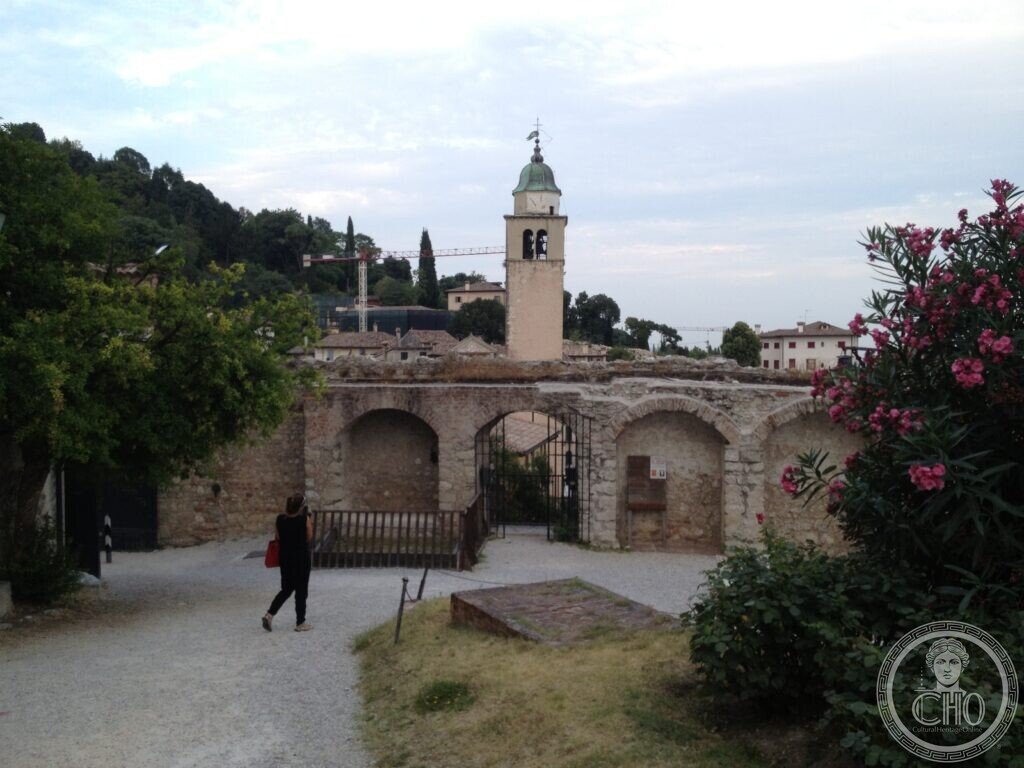 Arched stone wall and gate at the entrance to the Castle of Asolo, with a bell tower rising behind