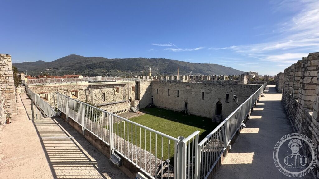 The grass courtyard of the Castello dell'Imperatore seen from the walkway on the walls, with hills beyond