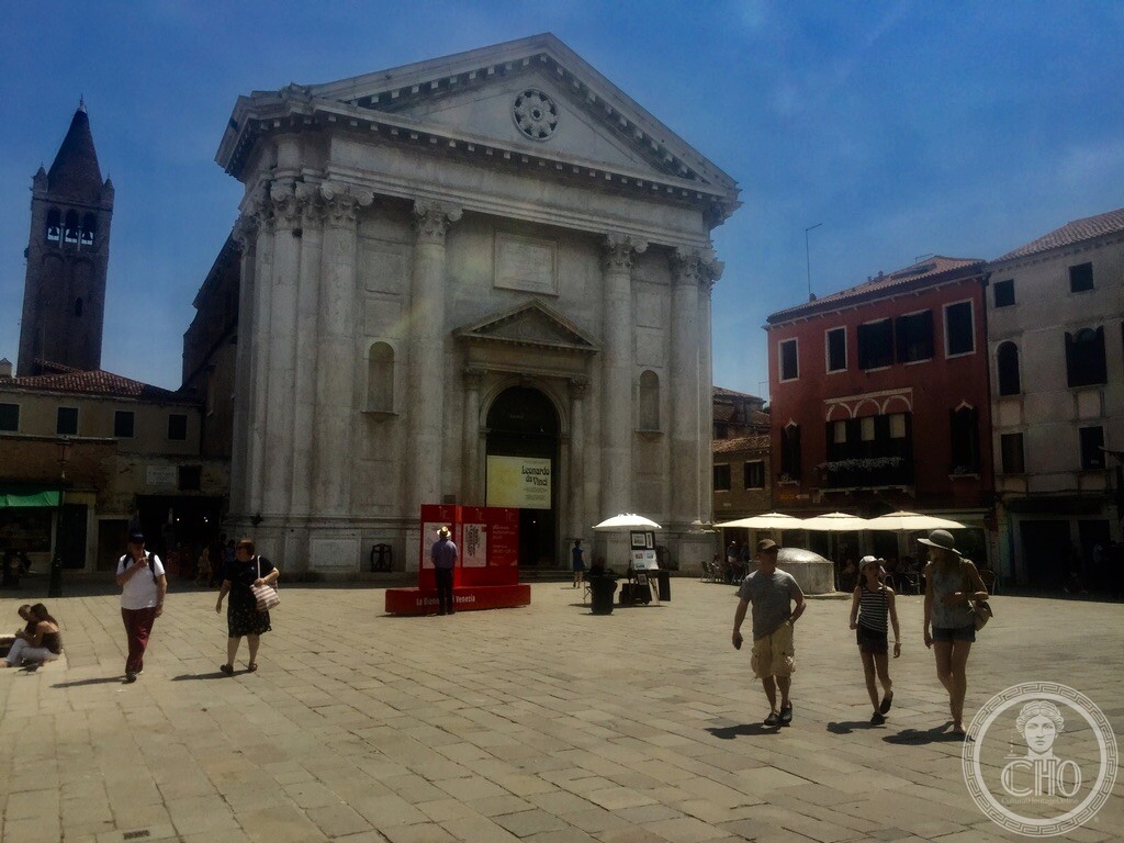 The classical facade of the church of San Barnaba in Venice with its brick bell tower seen across the campo