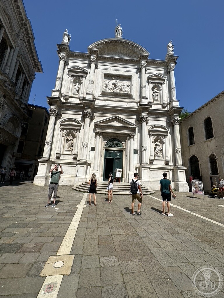 The eighteenth-century front of the church of San Rocco seen across the paved campo, statues of saints in niches and on the skyline
