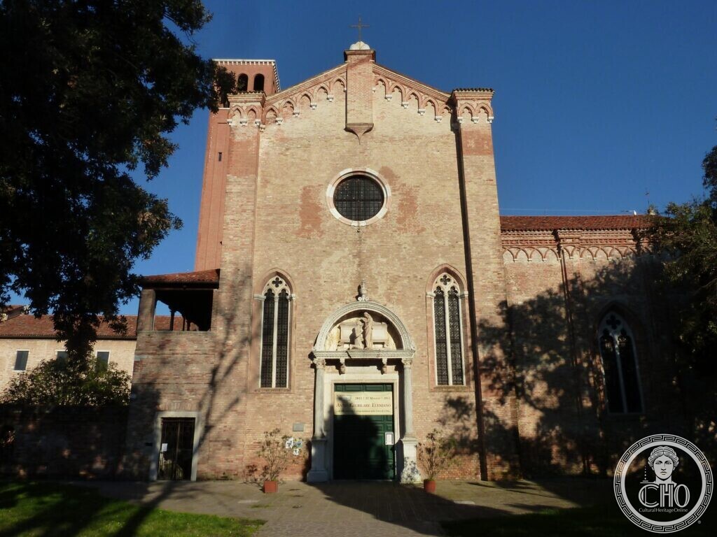 A brick Gothic church front with a round window, two tall pointed windows and a carved white stone portal, a brick bell tower behind