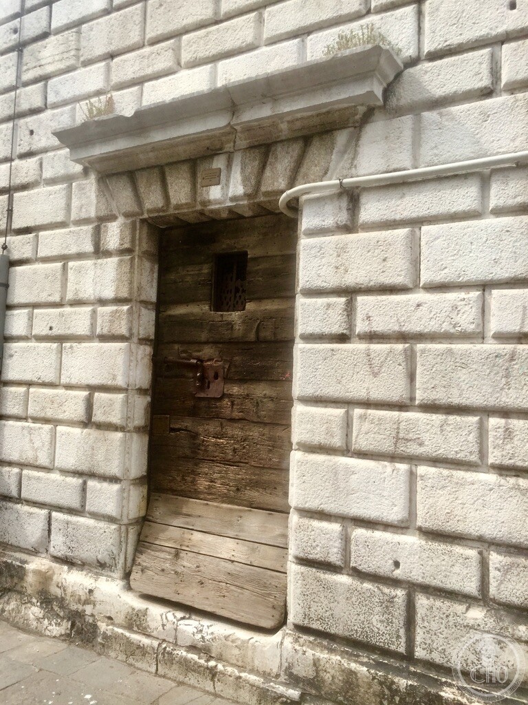 Heavy rusticated Istrian stone portal and weathered timber door with high-water protection boards at the base of Andrea Tirali’s bell tower at Chiesa dei Santi Apostoli in Venice