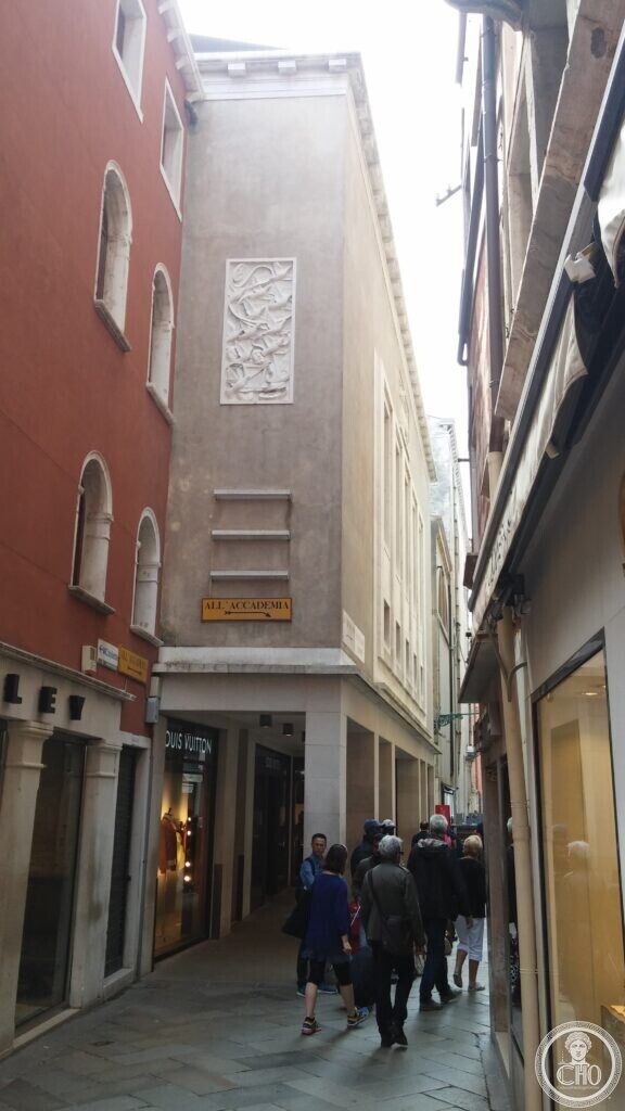 Narrow calle in Venice with the stone facade of the former Cinema Teatro San Marco, now a Louis Vuitton store, and a stone relief panel of doves