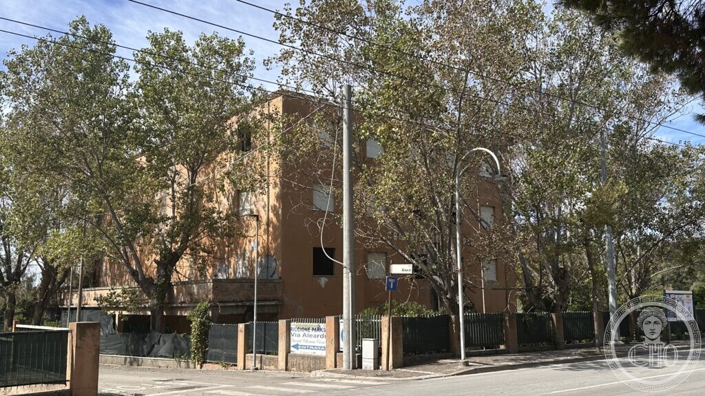 Full front elevation of the derelict Ex Colonia Adriatica in Riccione, with a Riccione Parks sign on Via Aleardi in front of it