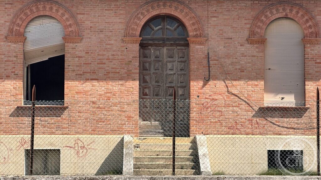 A brick facade with three round-arched openings, the central one a panelled wooden door