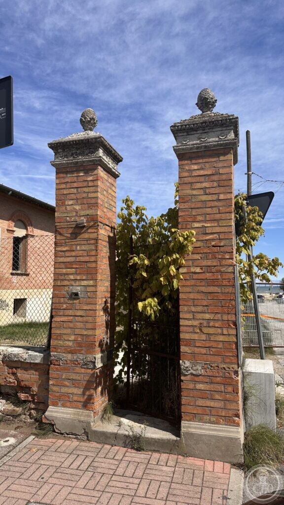 Two brick gate piers topped with carved stone pinecones, with an iron gate between them
