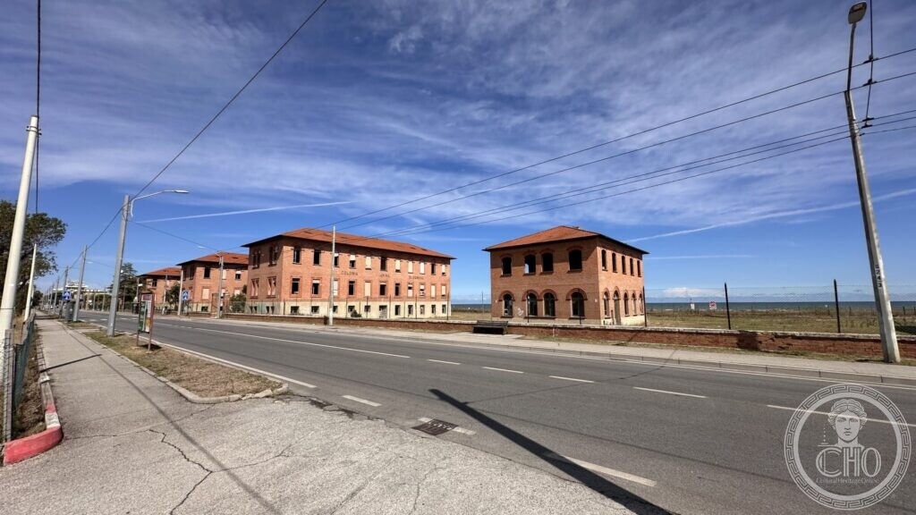 The brick pavilions of the colony seen from across the coast road, with the sea beyond