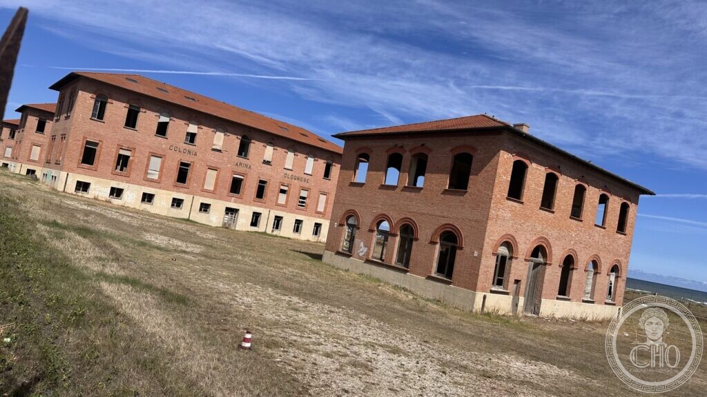 Two brick pavilions of the colony seen from a grassy rise, with the sea at the right