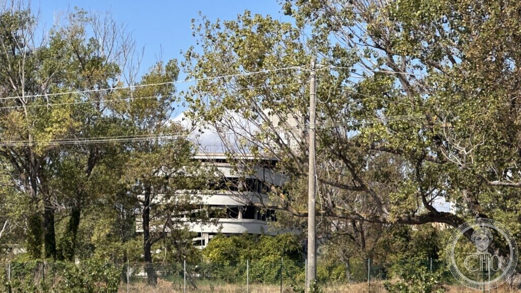 The upper floors of the colony seen through trees growing along the perimeter fence