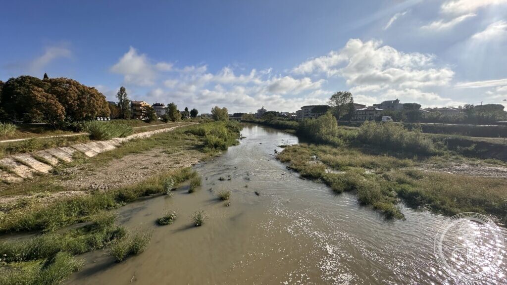 The straight diversion channel seen from the bridge, with grass islands in the low water and houses along the bank