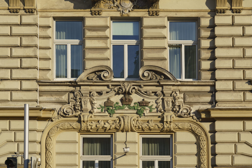 Carved cartouche over an arch on a rusticated facade, with three crowns on green laurel branches between stone scrolls, Rechte Wienzeile, Vienna