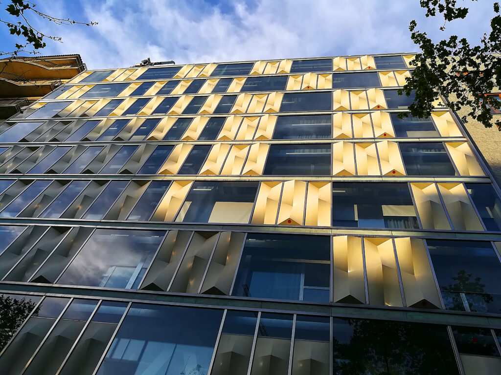 Office facade of reflective glass panels alternating with folded gold-tinted panels in a regular grid, Passeig de Gràcia 84, Barcelona