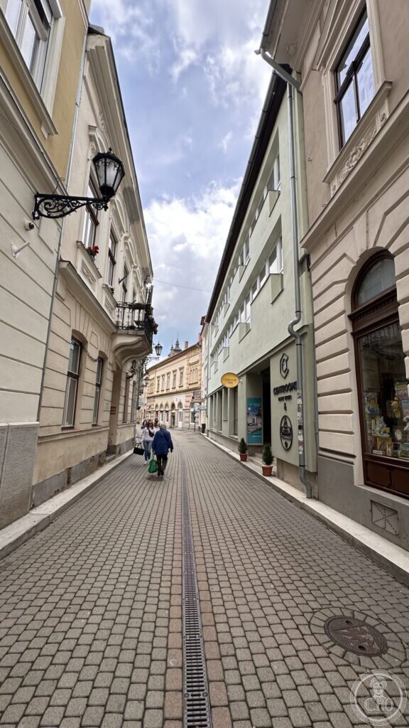 A narrow paved lane in Eger seen from its lower end, with a rusticated house front and an arched shop window on the right