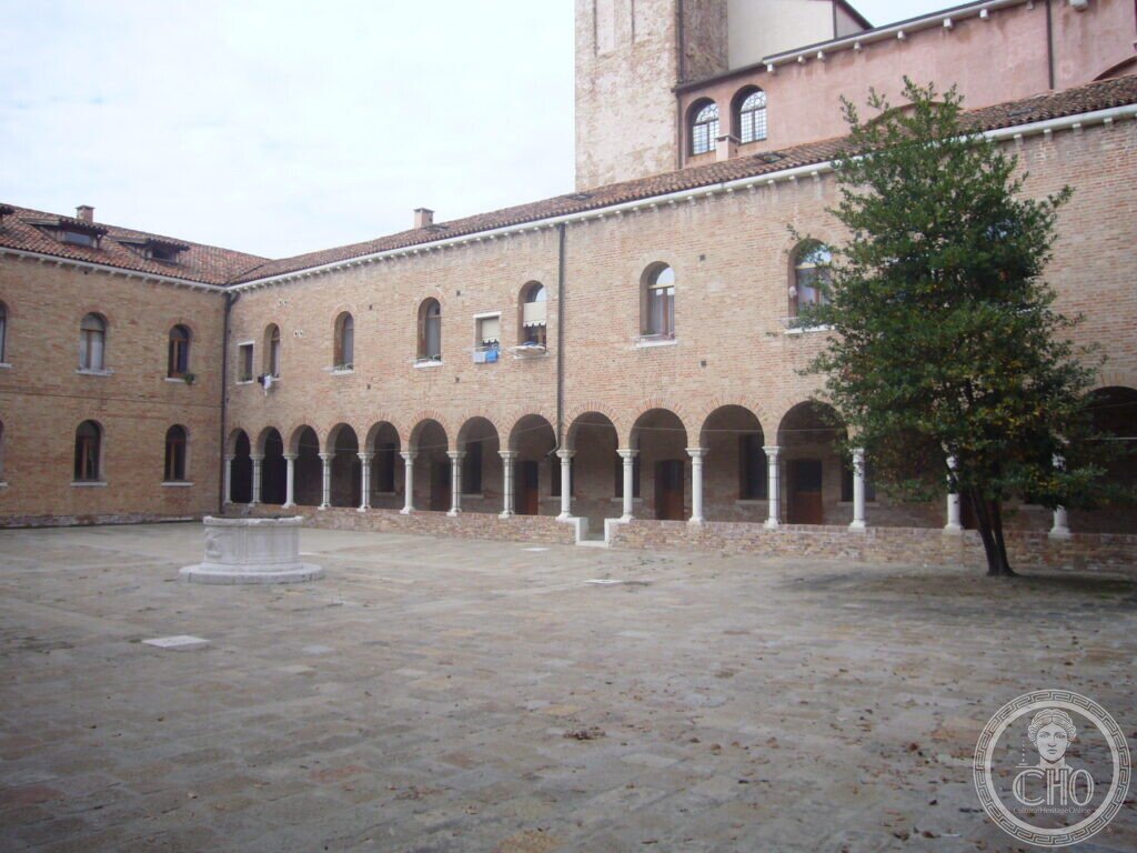 Courtyard of the cloister of Santi Cosma e Damiano with stone well-head, arcaded walk and the church bell tower behind