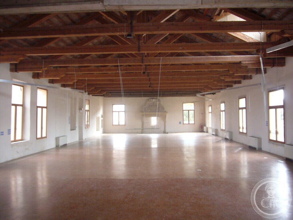 Restored upper hall of the former convent with timber roof trusses and a monumental stone fireplace