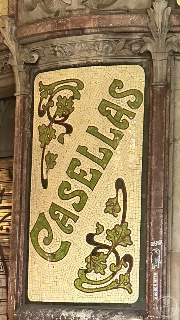 A mosaic panel spelling CASELLAS in green tesserae on a pale yellow ground, with curling leaves