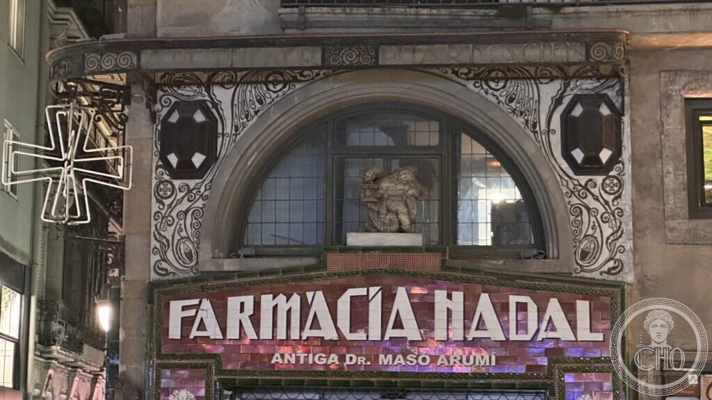 The illuminated sign FARMACIA NADAL, ANTIGA Dr. MASÓ ARUMÍ, under a semicircular arch with a sculpted figure