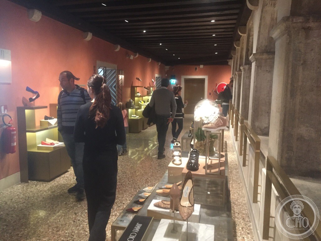 A shop corridor inside the Fondaco dei Tedeschi, with designer shoe displays along the historic arcade