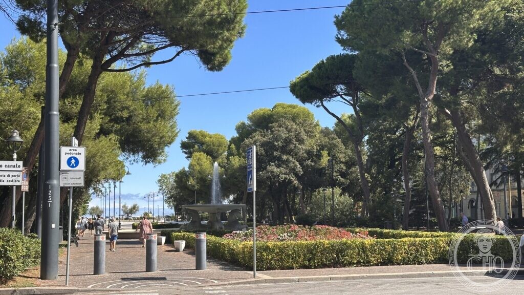 The entrance to the park with bollards and a pedestrian-zone sign, the fountain visible beyond