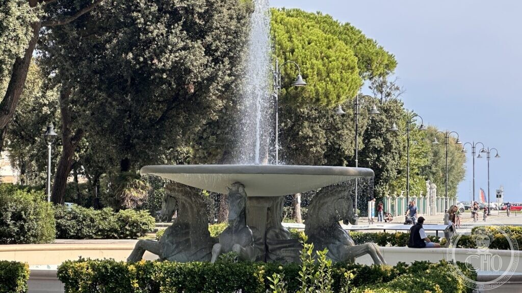 The fountain playing with a tall jet, the seafront promenade and lamp posts visible to the right
