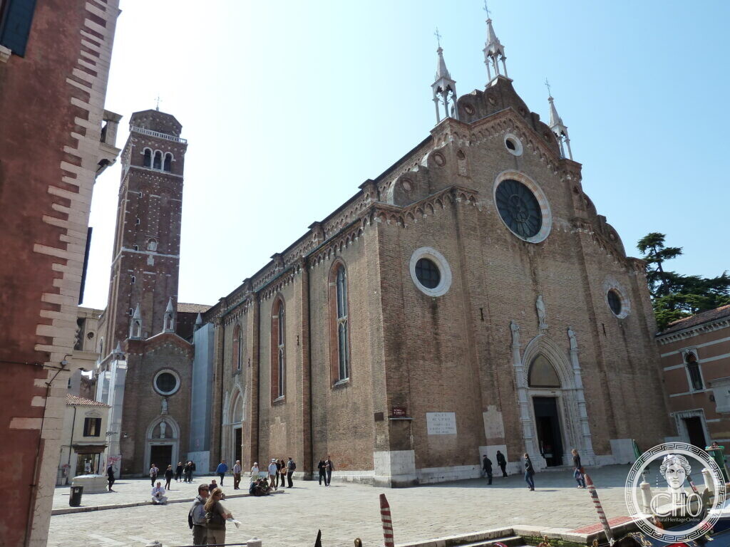 The brick Gothic front of the Frari basilica in Venice with its rose window and pinnacles, the fourteenth-century campanile rising behind, seen across Campo dei Frari