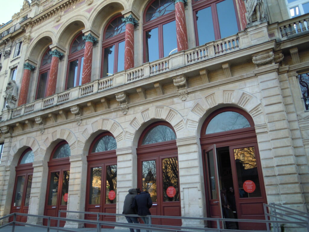 Stone arcade and upper loggia of the Gaîté Lyrique theatre, Paris, with red columns, Corinthian capitals and wine-red doors