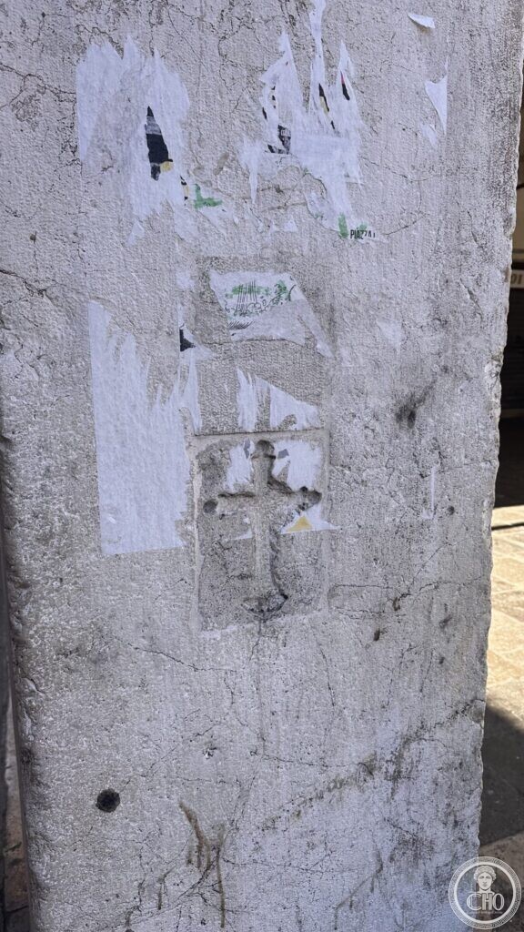 A weathered stone pillar with torn paper notices and a small cross carved in relief inside a square frame