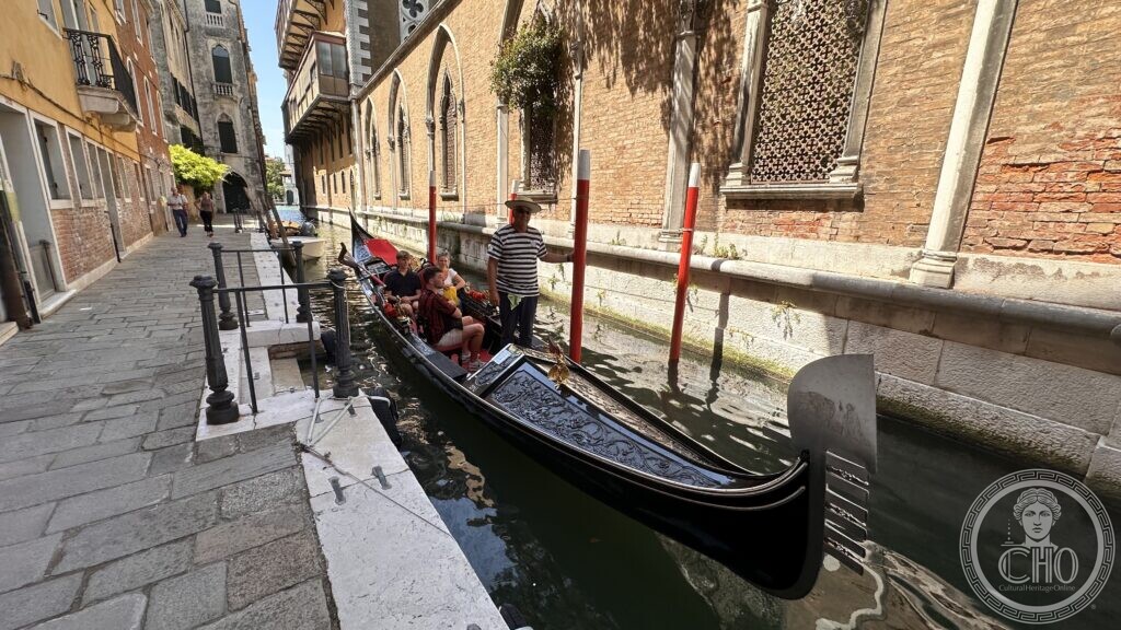 A gondola with passengers and gondolier moored in a narrow Venetian canal beside a Gothic brick facade